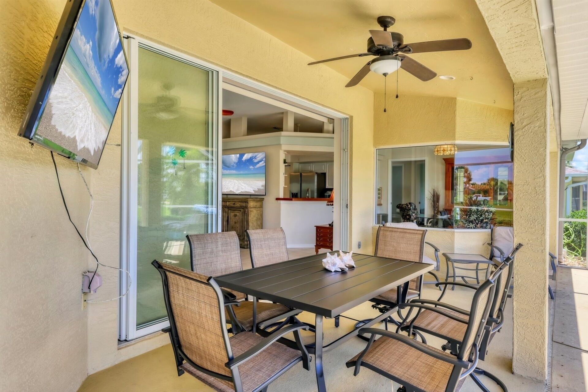 A covered patio with a dining table and chairs, a ceiling fan, and a view of the kitchen and backyard through glass doors.