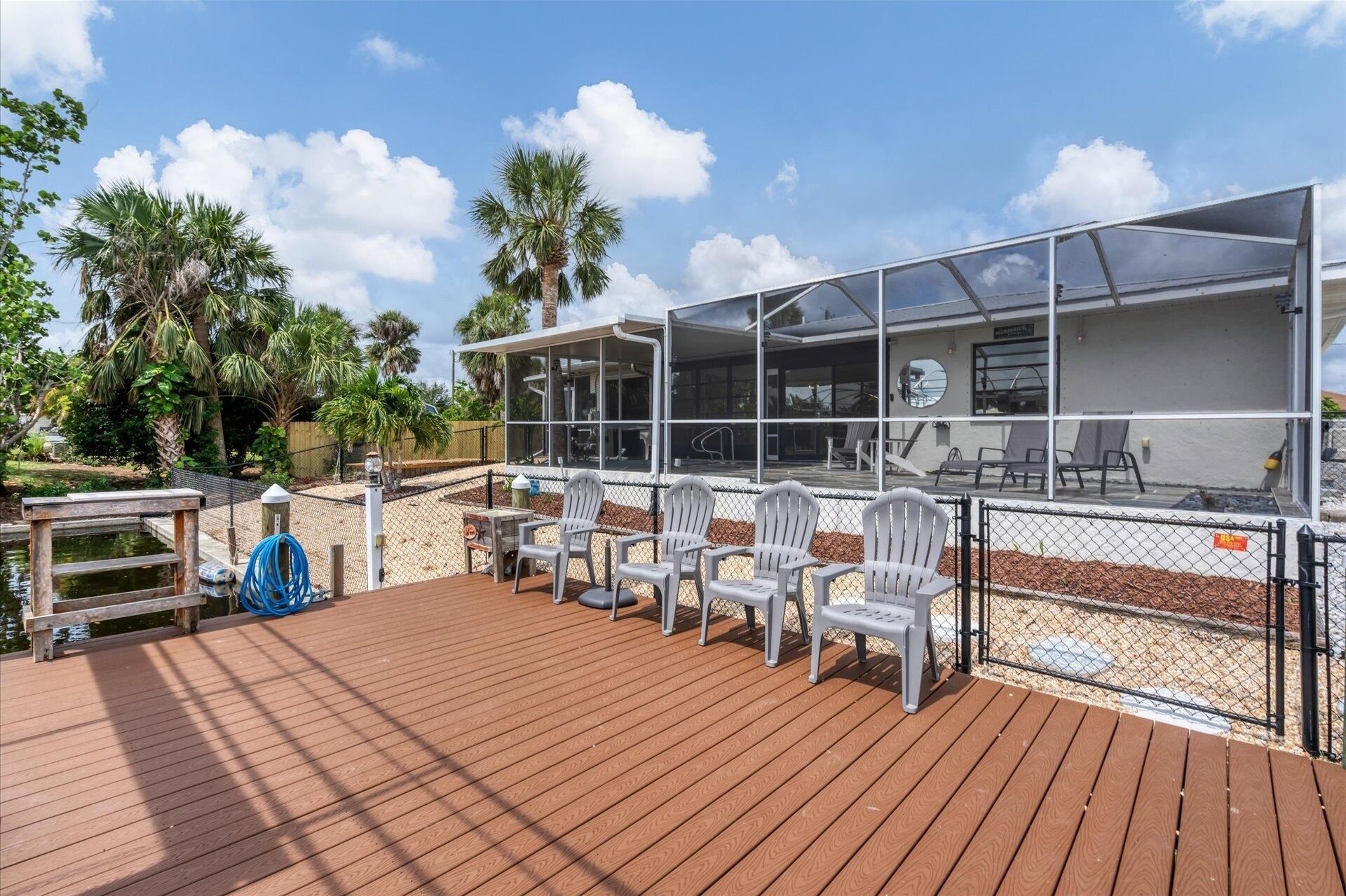 Ein überdachter Außenbereich mit Holzdeck, weißen Stühlen und einem Pool.