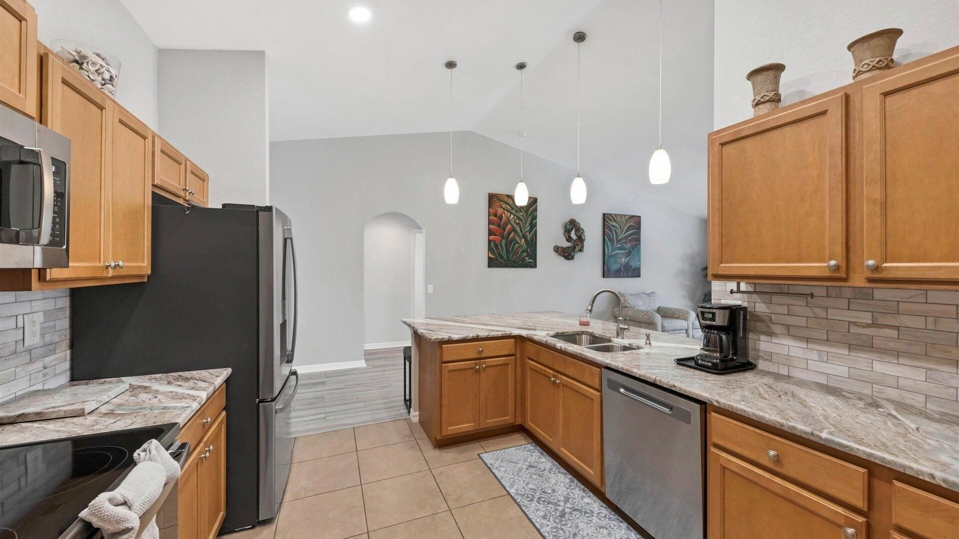 A modern kitchen with wooden cabinets, a stainless steel refrigerator, a built-in oven, a coffee maker, and pendant lighting.