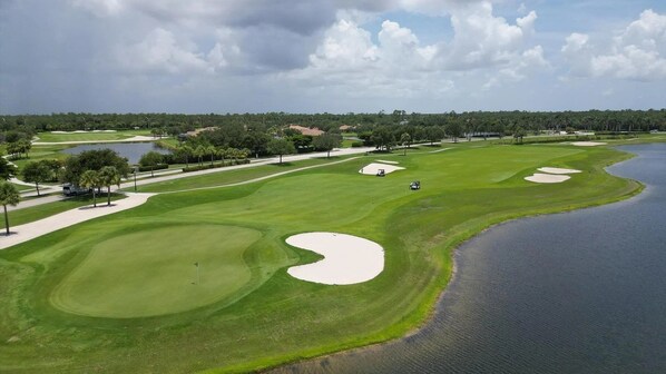 Un campo de golf con búnkeres de arena, una masa de agua y una carretera con vehículos.