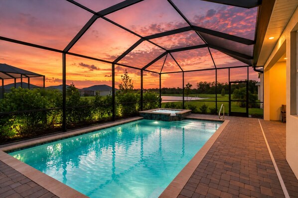 Una piscina con cerramiento de vidrio, rodeada de vegetación y vista al atardecer.