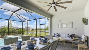A spacious patio with a dining table set for four, a ceiling fan, and a view of a swimming pool and greenery. - Heritage Landing Resort 4 Bedroom House Private Pool+Spa 4 Home (Punta Gorda)