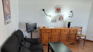 Ett vardagsrum med en soffa, ett soffbord, en tv på ett tv-bord, träskåp och konst på väggen.