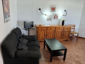 A living room with a sofa, a coffee table, a TV on a stand, wooden cabinets, and wall art. - Seafront Apartment with Balcony, Pool, Parking, and WiFi in Torredembarra (Torredembarra)