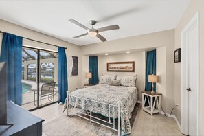 Ein Schlafzimmer mit Bett, Deckenventilator, einem Gemälde und Blick auf einen Pool.