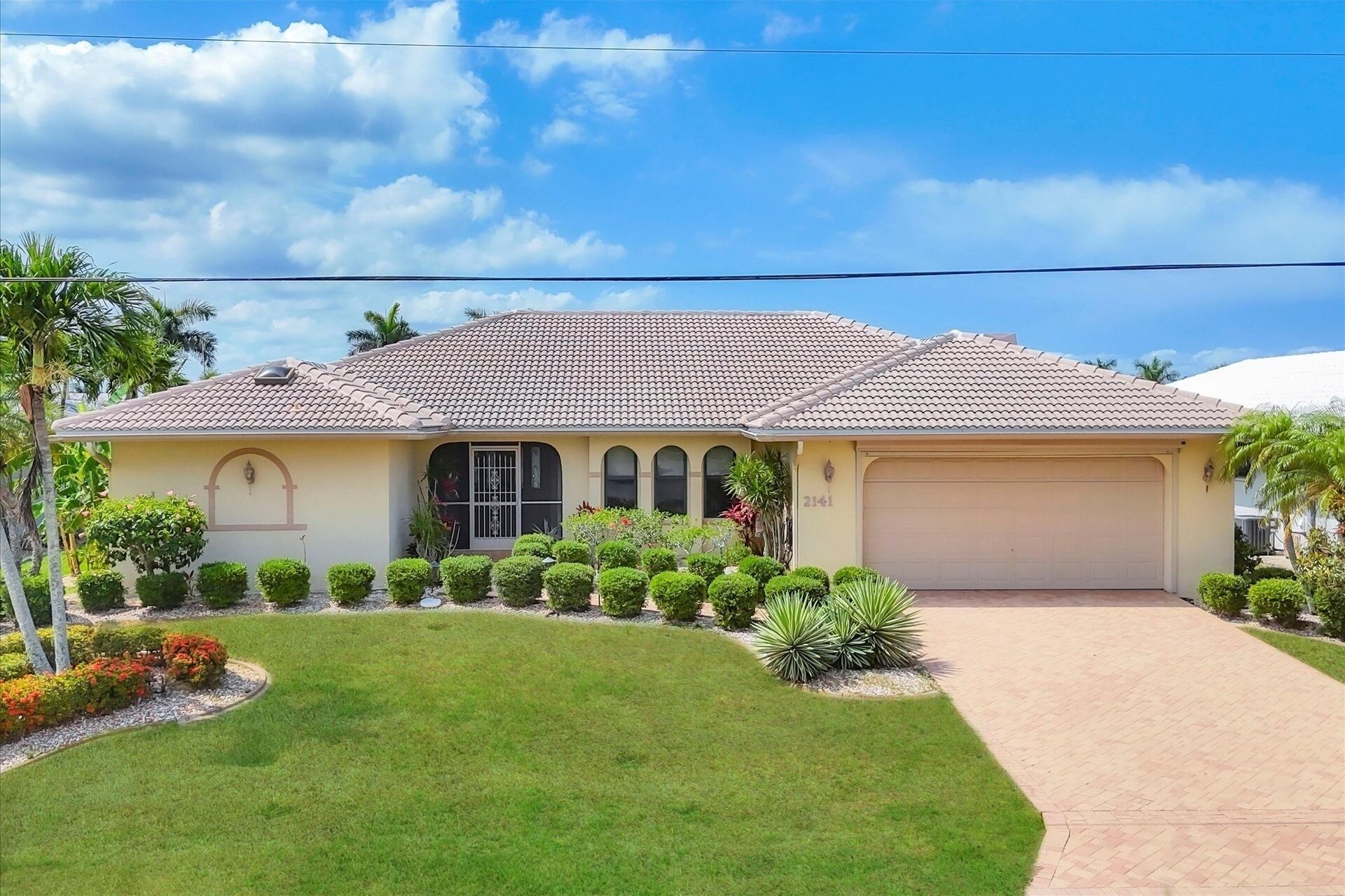 A single-story house with a tiled roof, a garage, and a well-maintained lawn with various shrubs and plants.