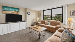 A living room with a large flat-screen TV, a beige sofa, a coffee table, and a window with a view of palm trees. - Anchorage Resort 3rd Floor 2 Bedroom Condo South/West Balconies 2 Condo (Siesta Key)