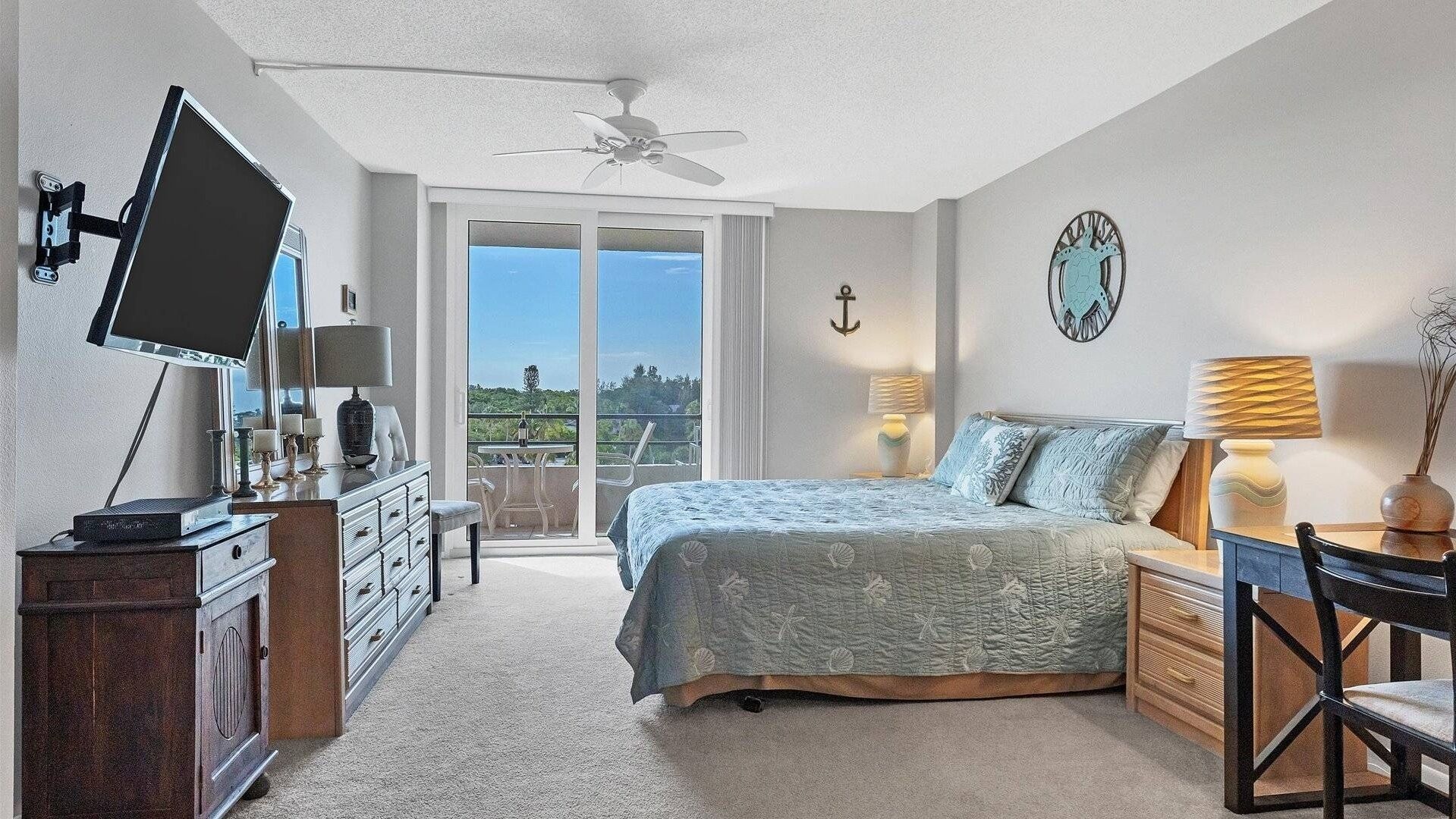 A bedroom with a bed, a desk, a television, and a balcony with a view.