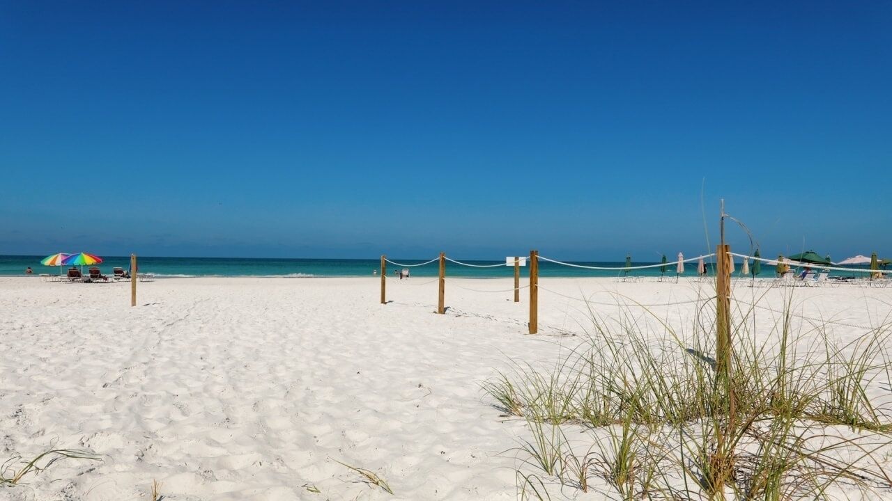 Une plage avec une barrière faite de cordes, un parasol coloré et un ciel d’un bleu limpide.