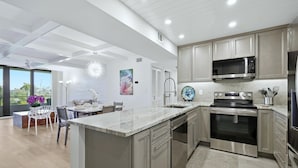 Een moderne keuken met roestvrijstalen apparatuur, een eethoek met witte stoelen en een groot raam met uitzicht.