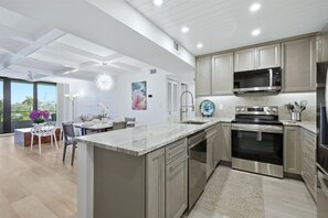 A modern kitchen with stainless steel appliances, a dining area with white chairs, and a large window offering a view.