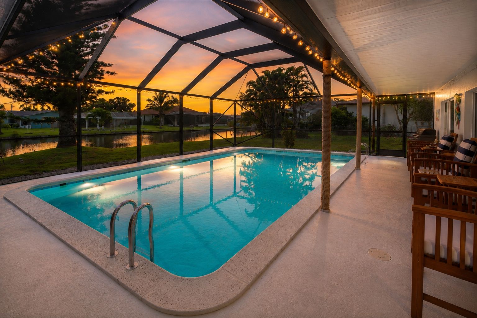 A swimming pool with a glass enclosure, surrounded by outdoor furniture and a view of a sunset.