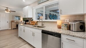 A modern kitchen with white cabinetry, granite countertops, a dishwasher, and a coffee maker. - Cape Coral 3 Bedroom Private Pool Home - Canal Access 3 Home (Cape Coral)