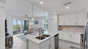 A modern kitchen with white cabinetry, a central island with a sink, and a dining area with a view of the outdoors. - 30-night Min 3 Bdrm 2nd Floor Heritage Landing Golf Club Transfer Included! 3 Bedroom Condo (Punta Gorda)