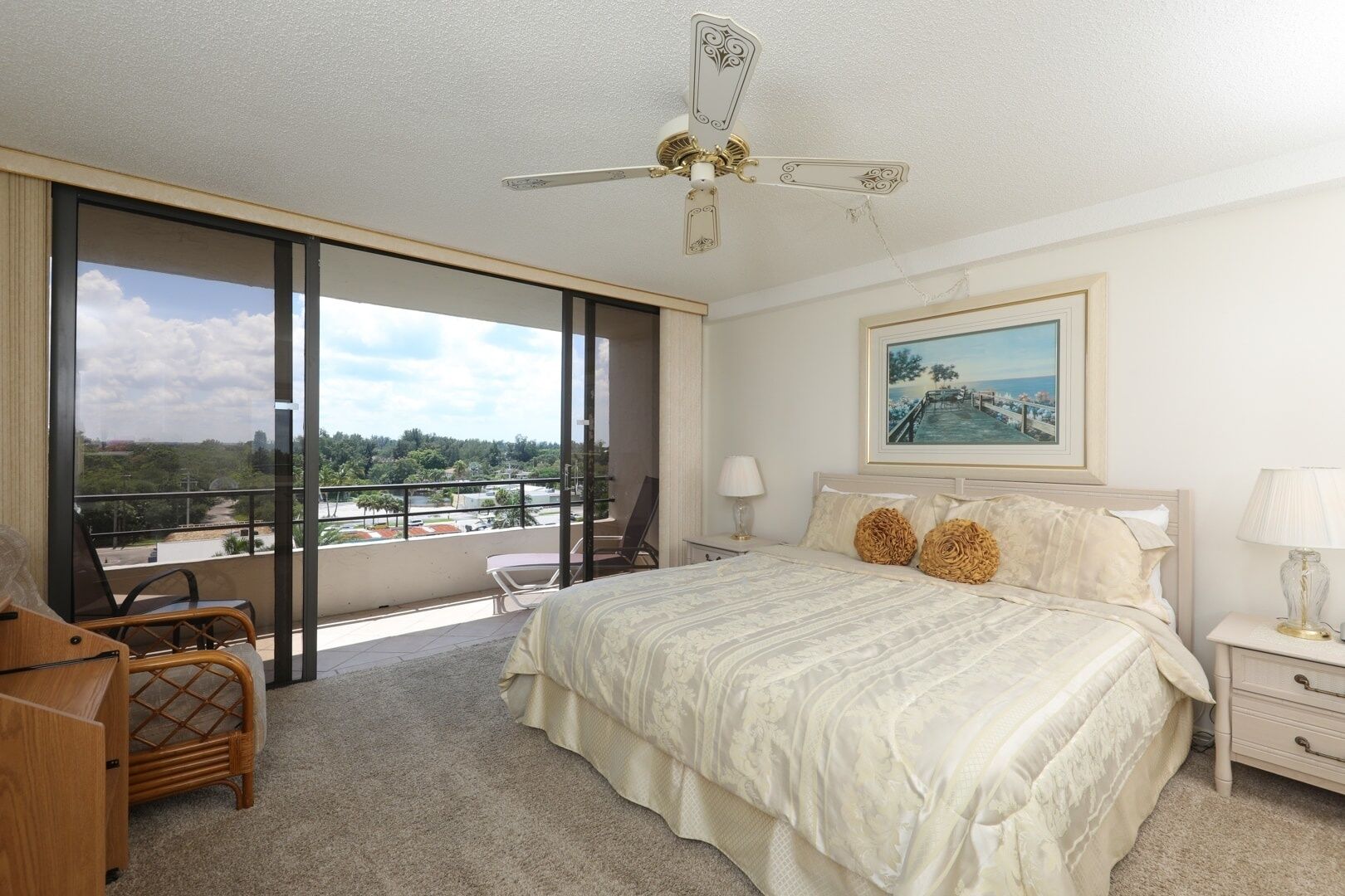 A hotel room with a large bed, a balcony with a view, a ceiling fan, and a painting on the wall.