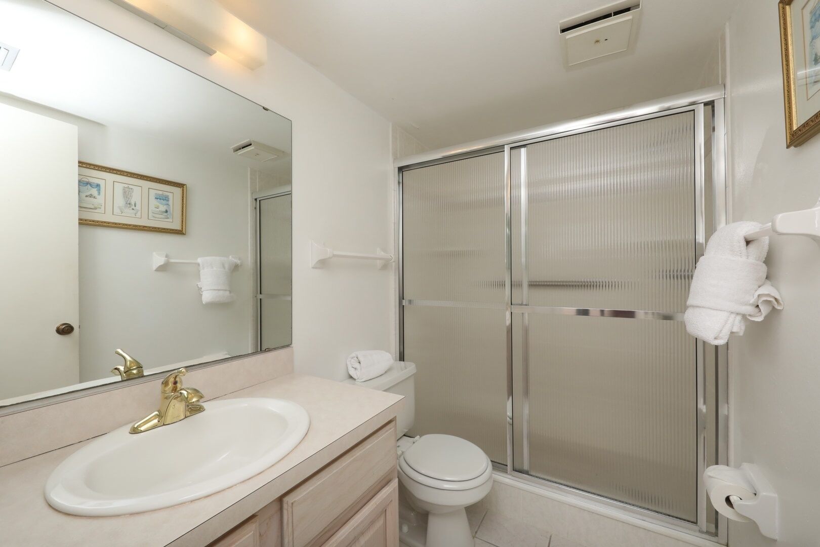 A modern bathroom with a large mirror, a sink, a toilet, and a shower enclosure.