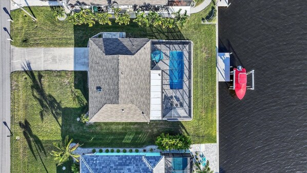 Ovenudblik over en ejendom med swimmingpool, overdækket terrasse og bådebro.