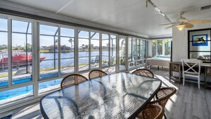 Tilava huone, jossa on suuri lasiseinä, josta avautuu näkymä vesistöön, ruokailutila, jossa on punottuja tuoleja, ja kattotuuletin.
