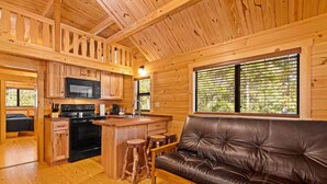 Un interior de cabaña acogedor con cocina, comedor y sala de estar con sofá de cuero.