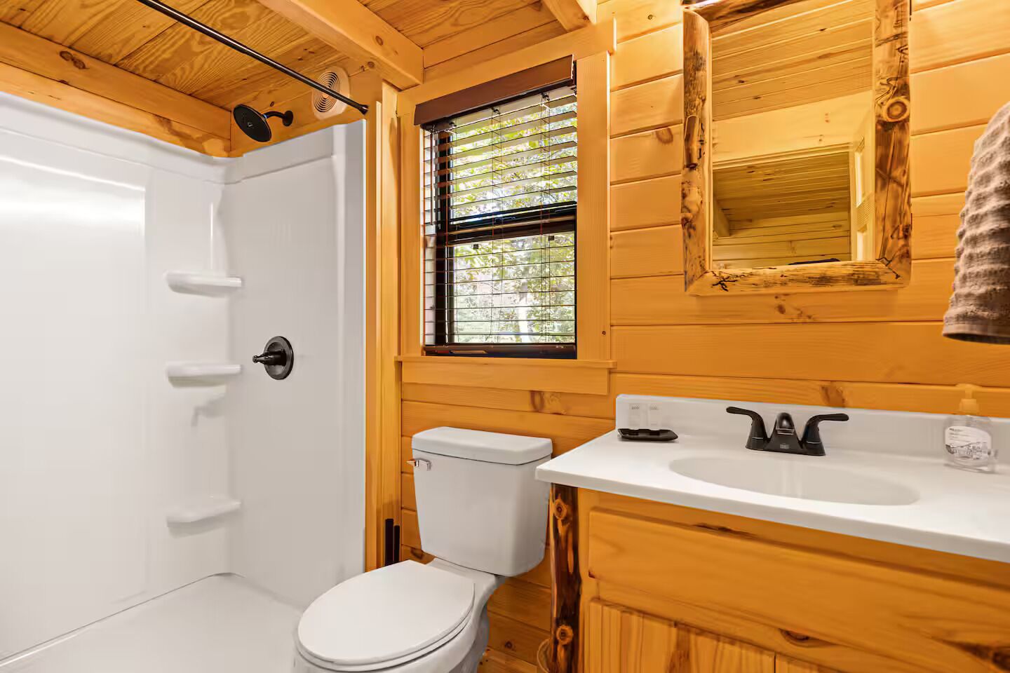 A wooden cabin bathroom with a white toilet, a shower, and a sink with a mirror above it.