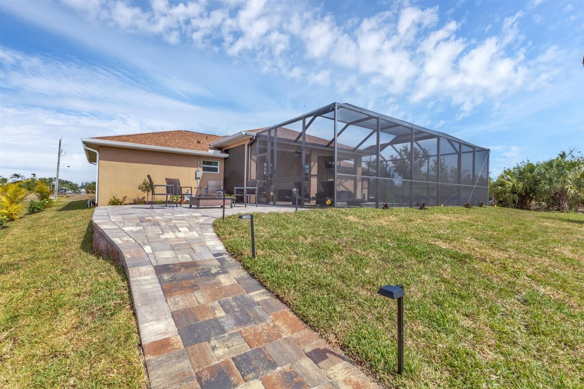 A house with a covered patio area, a paved walkway, and a grassy yard.