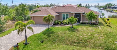A single-story house with a tiled roof, a front porch, and a well-maintained lawn with palm trees.