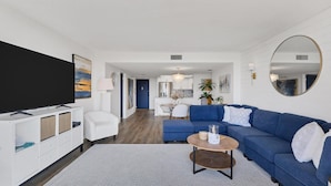 A modern living room with a large flat-screen TV, a blue sofa, a coffee table, and a dining area with a white table and chairs. - Anchorage Resort Siesta Key 2 Bedroom 6th Floor Condo Beach Access 2 Condo (Siesta Key)