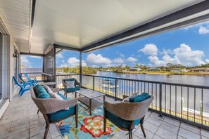 A covered outdoor area with wicker furniture, a colorful rug, and a view of a lake and distant buildings. - Port Charlotte 4 Bedroom Pool Vacation Home on Canal 4 Home (Port Charlotte)