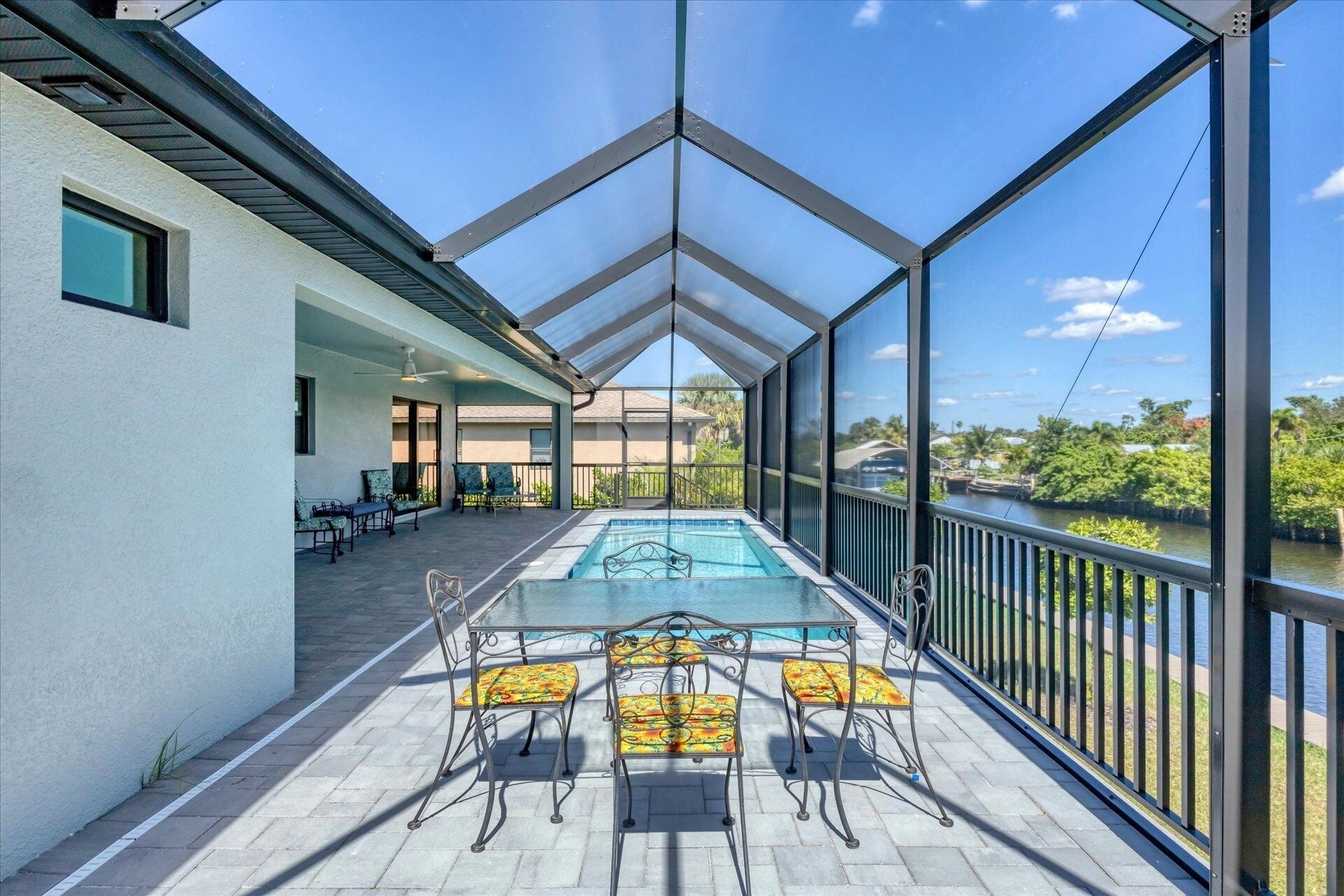 A covered outdoor swimming pool with chairs and tables, a view of a river, and a building with a white exterior.
