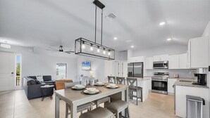 A modern kitchen with white cabinets, stainless steel appliances, and a dining area with a wooden table and bar stools. - Punta Gorda 4-Bedroom Private Pool Home on Canal 4 Home (Punta Gorda)