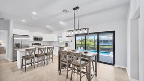 A modern kitchen with white cabinets, stainless steel appliances, and a dining area with wooden chairs and a table. - Punta Gorda 4-Bedroom Private Pool Home on Canal 4 Home (Punta Gorda)