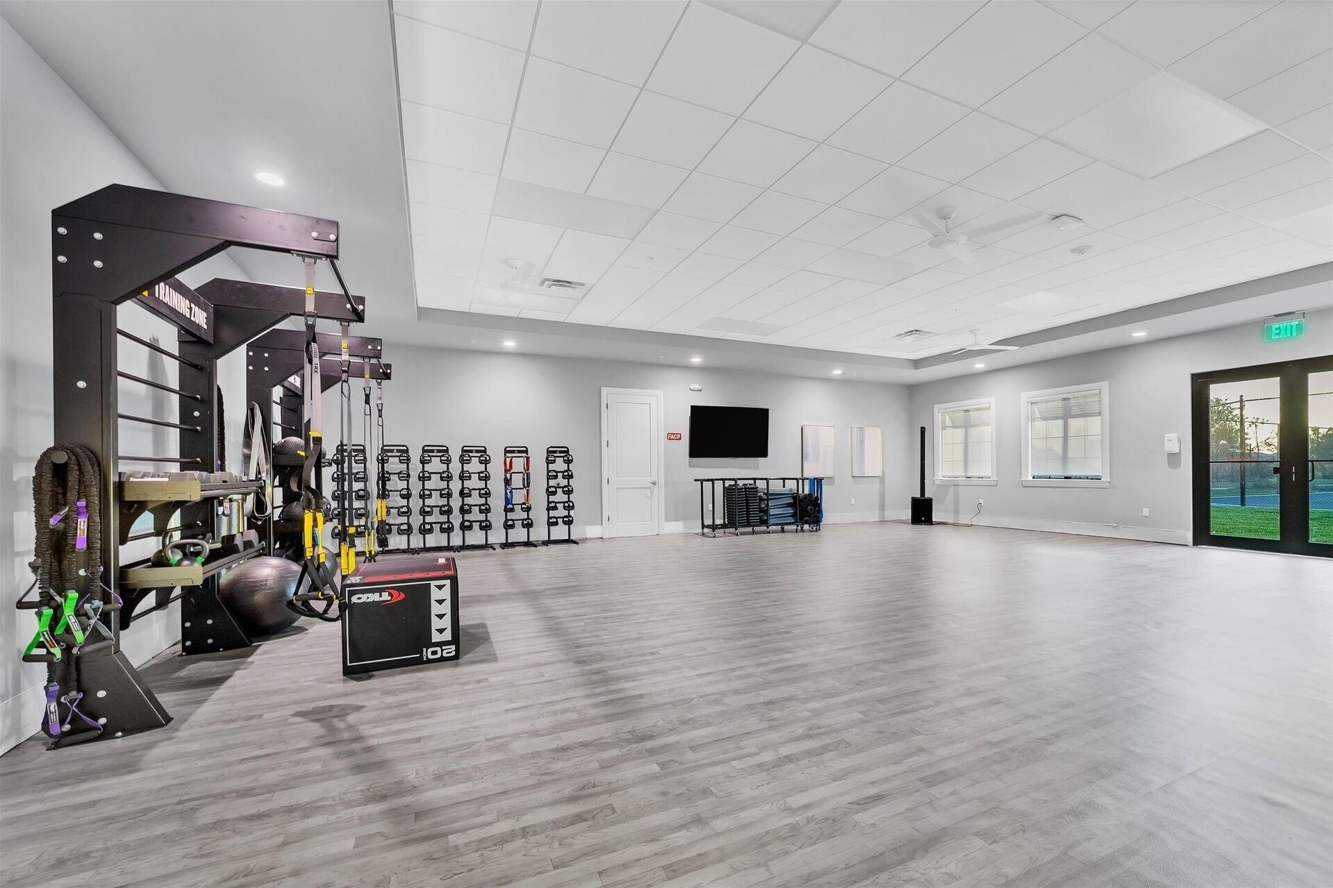 A spacious gym with various exercise equipment, a television, and a large window providing a view of the outdoors.