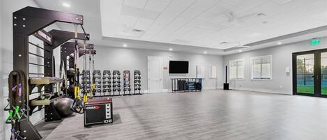 A spacious gym with various exercise equipment, a television, and a large window providing a view of the outdoors.