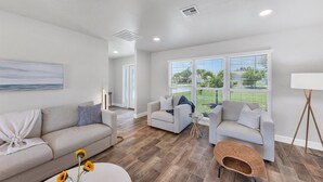 A spacious living room with a large window, a sofa, a chair, and a small table with a vase of sunflowers. - Punta Gorda Isles 2-Bedroom Private Pool Home on Canal with Dock 2 Home (Punta Gorda)