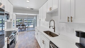 A modern kitchen with white cabinets, stainless steel appliances, and a large window overlooking a pool area. - Punta Gorda Isles 2-Bedroom Private Pool Home on Canal with Dock 2 Home (Punta Gorda)