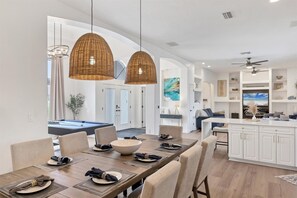 A modern dining area with a pool table, two large wicker pendant lights, and a kitchen with white cabinetry and a large island. - Punta Gorda 3-Bedroom Canalfront Vacation Home with Dock 3 Home (Punta Gorda)
