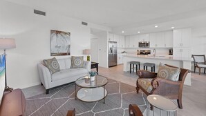 A spacious living area with a sofa, coffee table, and chairs, a kitchen with white cabinets and modern appliances, and a dining area with stools. - Heritage Landing Golf Club 2 Bedroom Condo 30 Night Minimum 2 Condo (Punta Gorda)