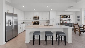 A modern kitchen with white cabinetry, stainless steel appliances, and a central island with bar stools. - Heritage Landing Golf Club 2 Bedroom Condo 30 Night Minimum 2 Condo (Punta Gorda)