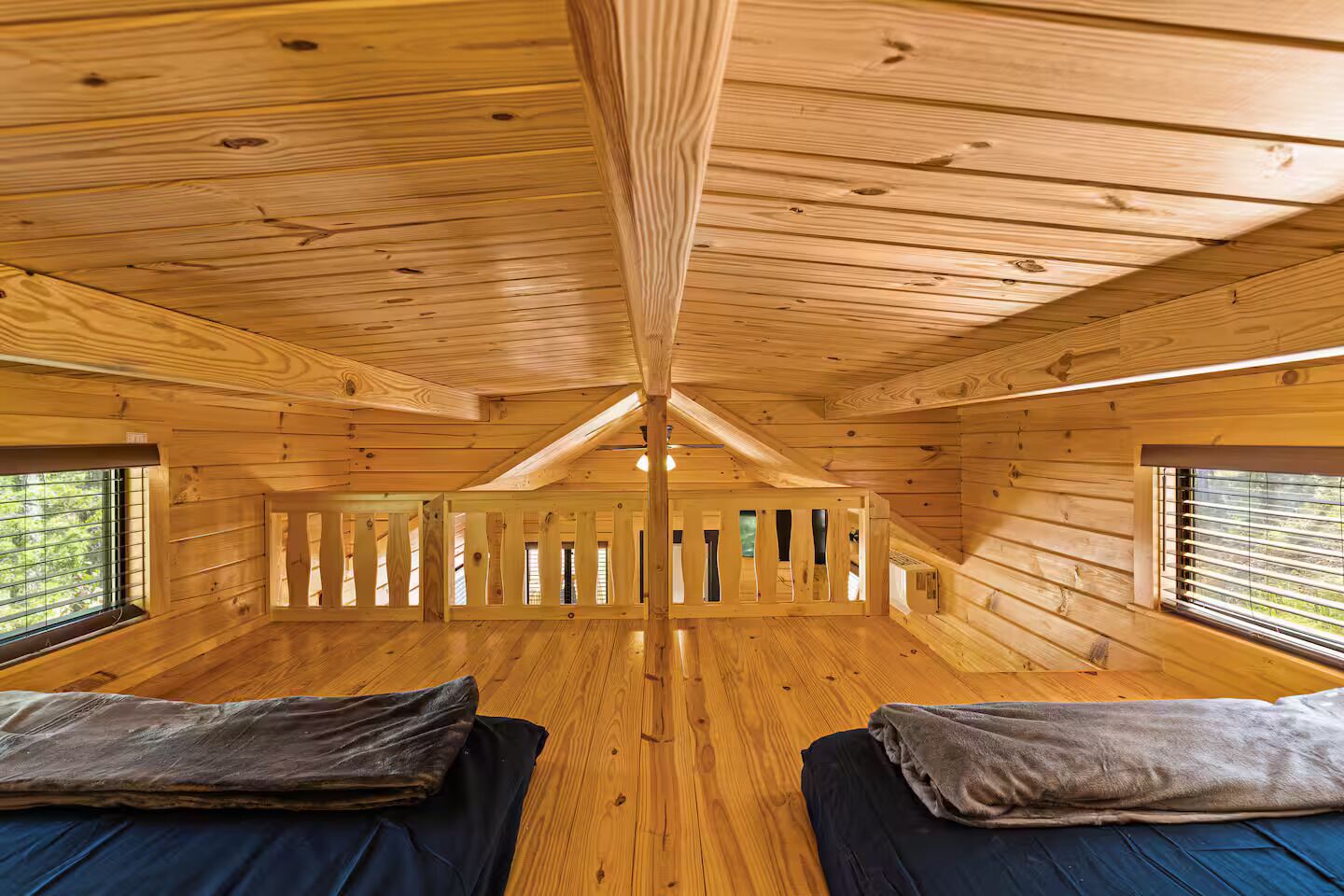 Interior de una cabaña con paredes de madera, techo inclinado y dos camas con almohadas.