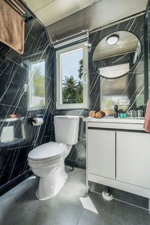 A modern bathroom with a toilet, sink, and a window with a view of palm trees. - Apple House Charming 1-bedroom cabin with AC in Tambon Choeng Thale (Tambon Choeng Thale)