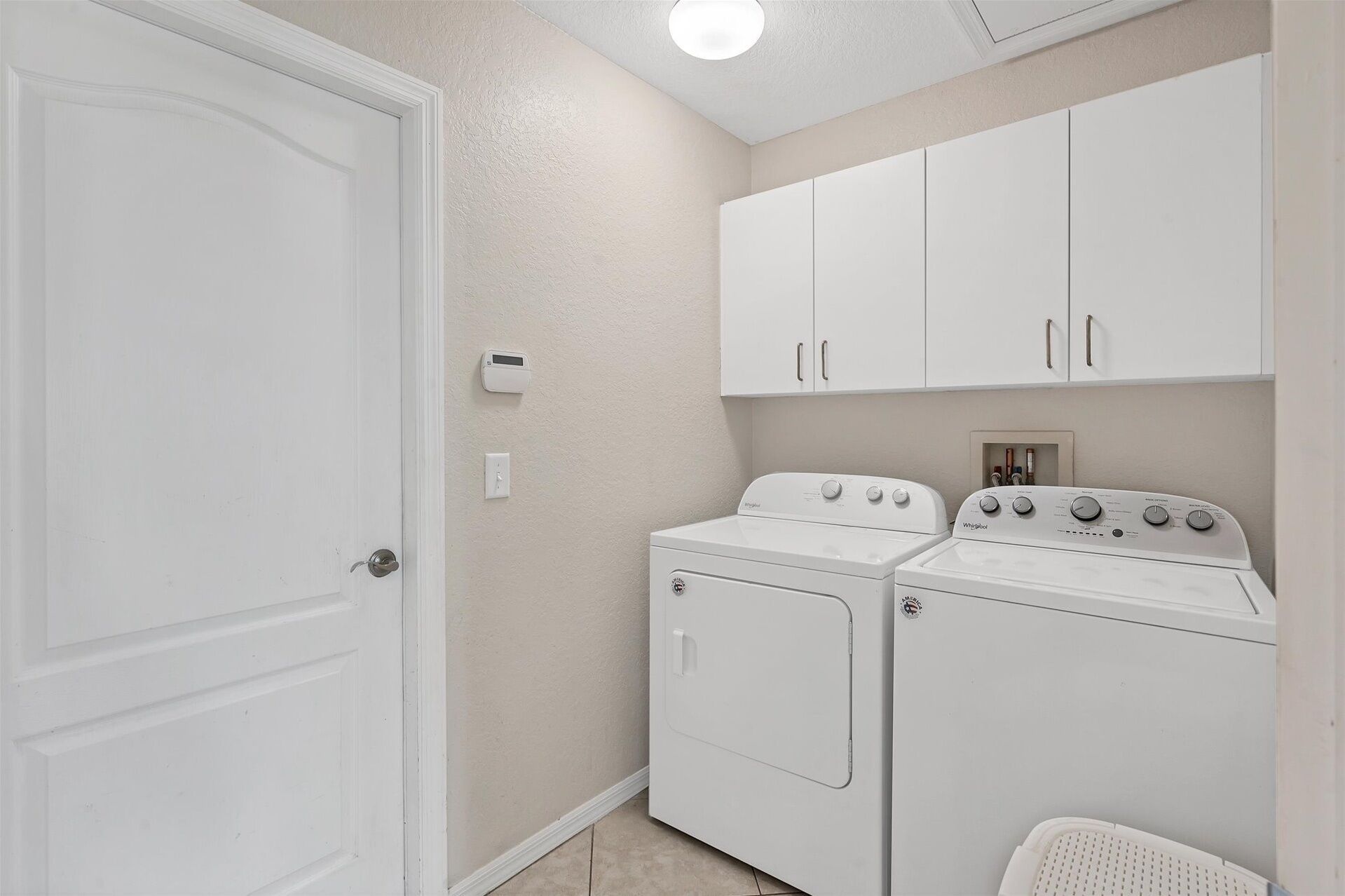 A laundry room with a washer and dryer, white cabinets, and a door.