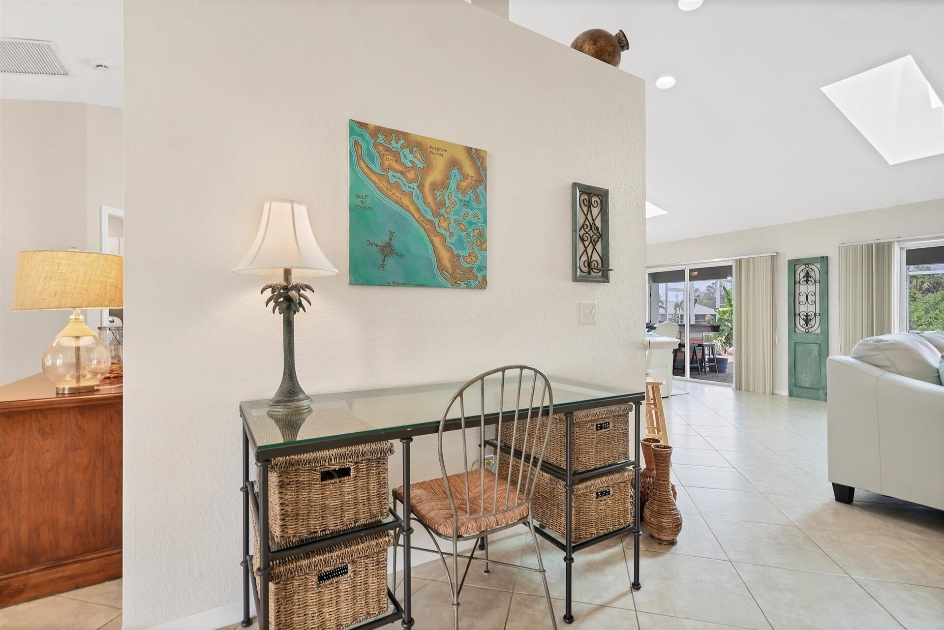 A modern living room with a glass-top dining table, wicker baskets, a metal chair, and a map on the wall.