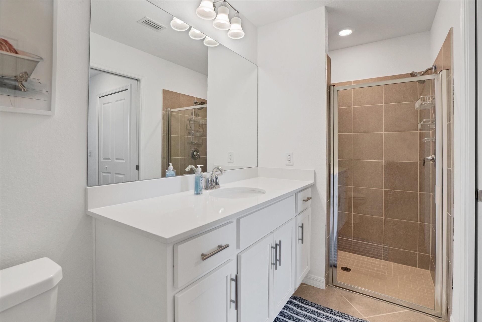 Une salle de bain moderne avec un meuble-lavabo blanc, un grand miroir et une douche à parois de verre.