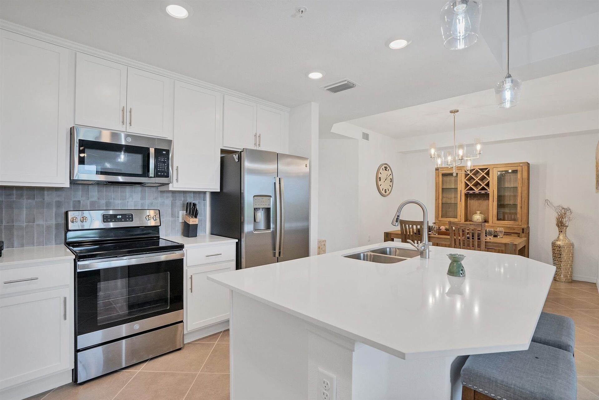 A modern kitchen with white cabinetry, stainless steel appliances, a large island with a sink, and a dining area with a wooden table and chairs.