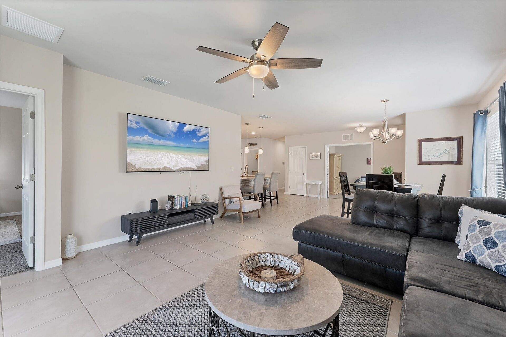 A spacious living room with a ceiling fan, a large flat-screen TV, a leather sofa, and a coffee table with a decorative bowl.