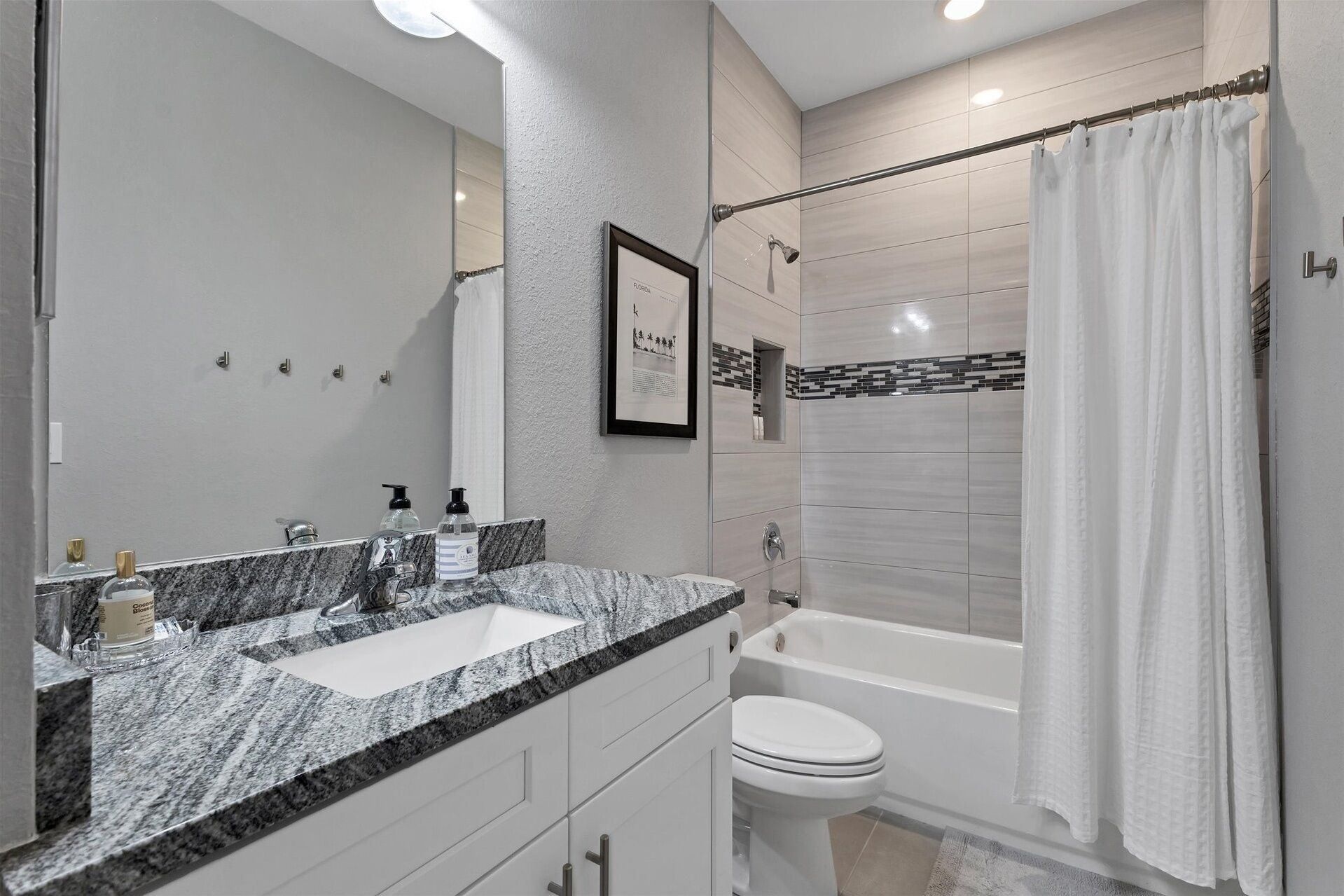 Un baño moderno con encimera de granito, un lavabo blanco, inodoro y bañera.