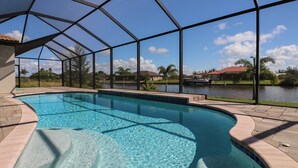 A swimming pool with clear blue water, surrounded by a covered area with a view of a lake and houses in the background. - South Gulf Cove 3 Bedroom Canal Pool Home 3 Home (Port Charlotte)