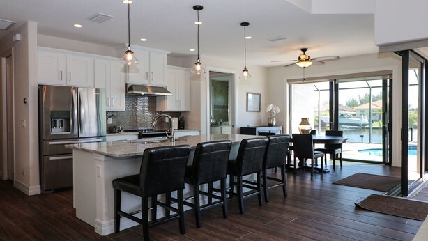 A modern kitchen with a central island, bar stools, stainless steel appliances, pendant lighting, and a view of a swimming pool through large glass doors. - South Gulf Cove 3 Bedroom Canal Pool Home 3 Home (Port Charlotte)