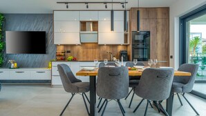 A modern kitchen with a dining area, featuring a large flat-screen TV, wooden cabinets, and a dining table with chairs. - Villa Polaris by Villas Guide (Pula)