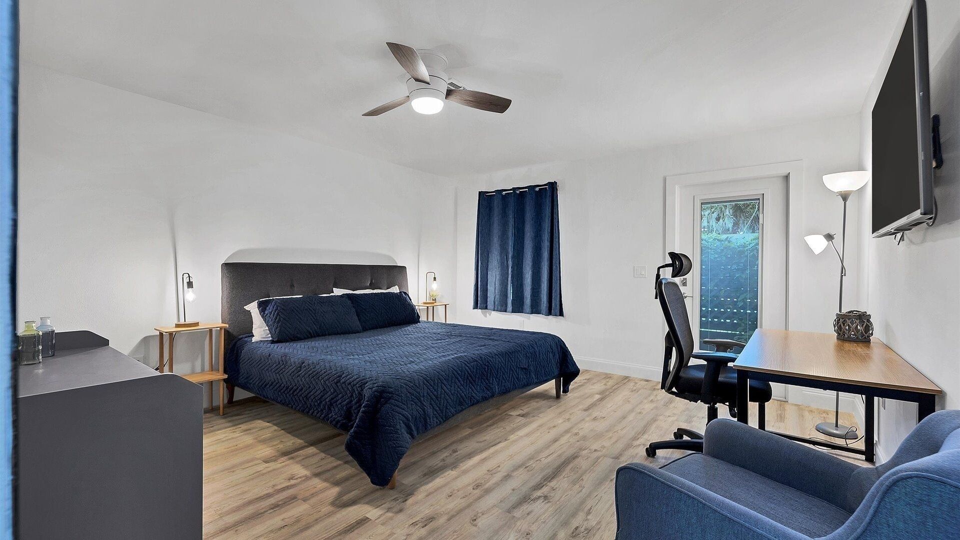 Une chambre moderne avec un lit, un bureau, une chaise et un ventilateur de plafond.